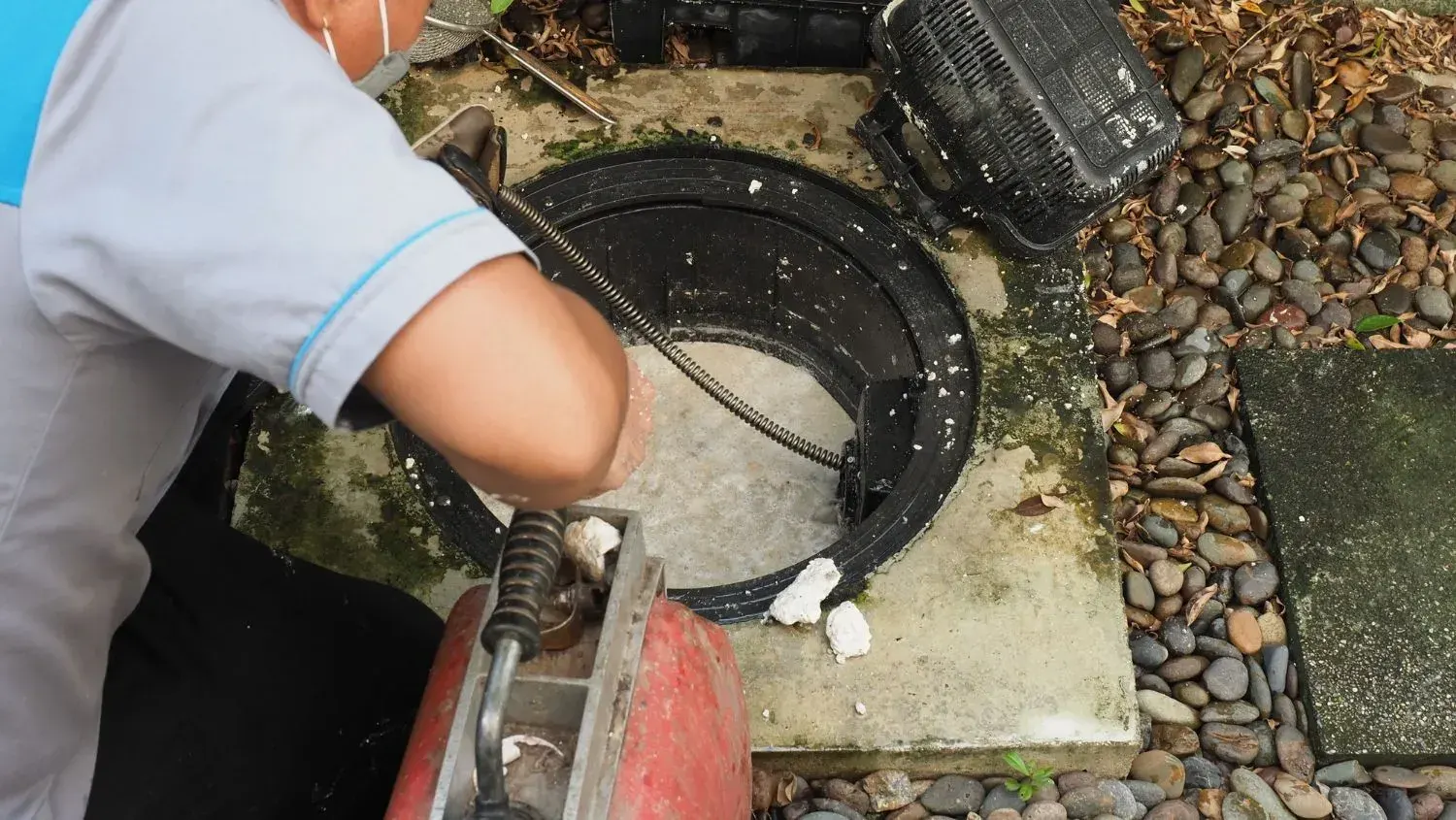 Technician feeding a drum machine drain snake cable into an outdoor floor drain