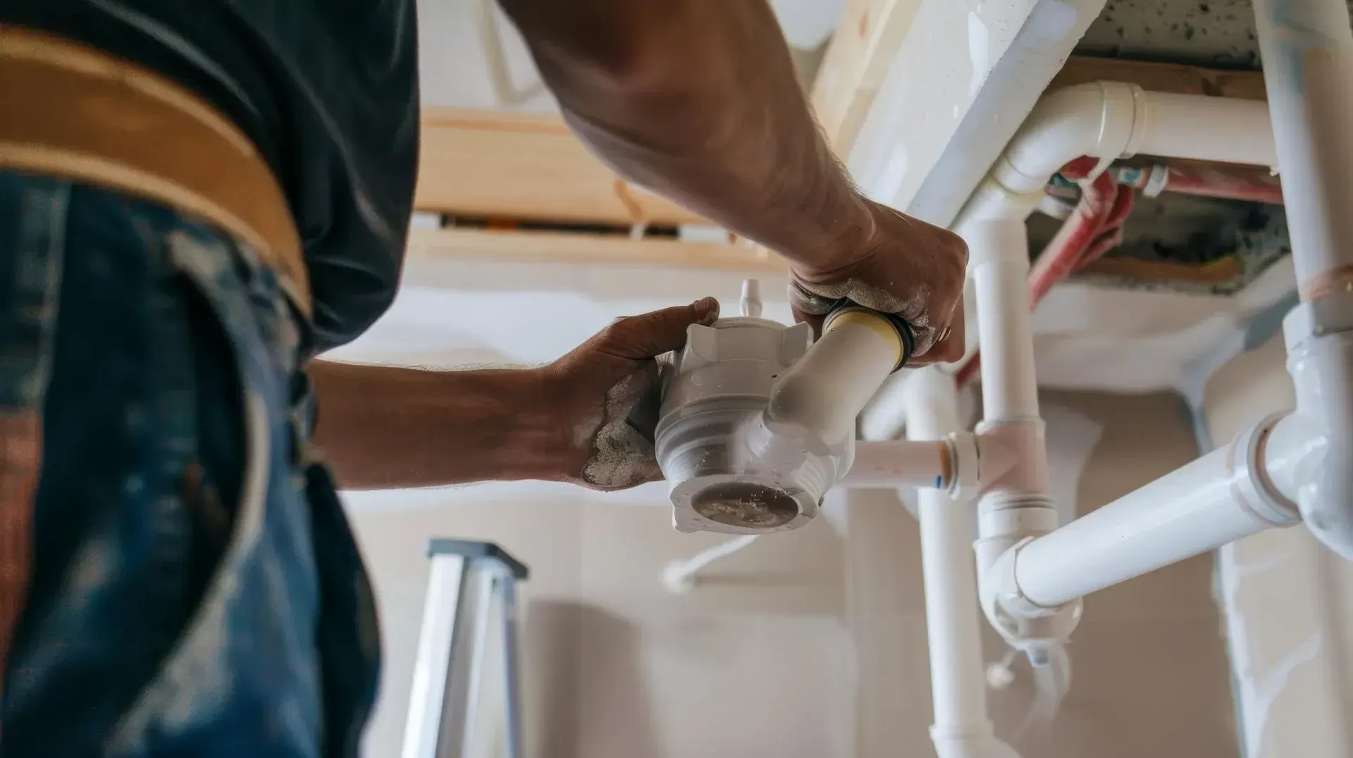 Plumber fitting a white PVC drain trap onto new pipework beneath a sink