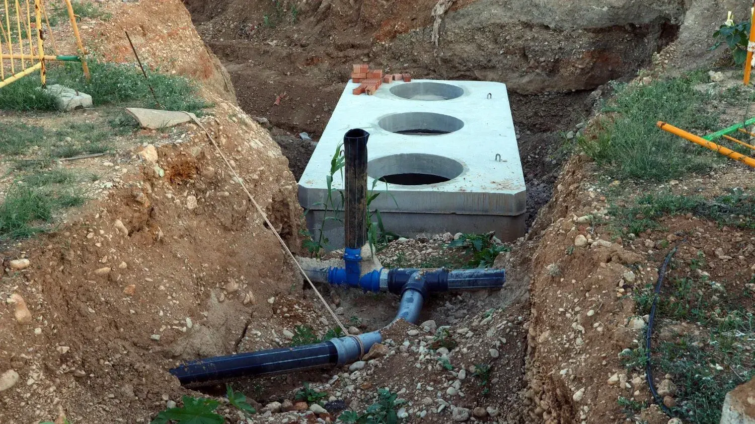 Concrete septic tank set in an excavated trench with new black and blue sewer pipe connections